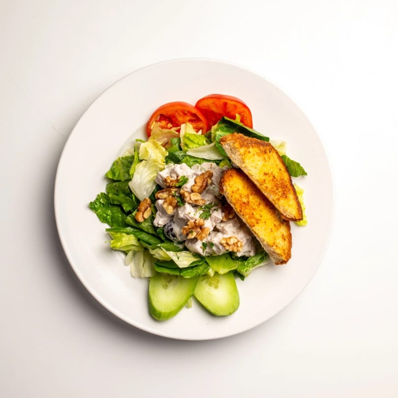 Chicken salad with walnuts, lettuce, tomato, cucumber, and toasted bread on a white plate.