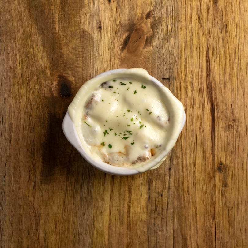 A white bowl of French onion soup with melted cheese and parsley on a wooden table.