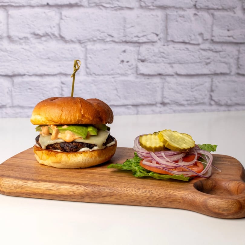 A Red Onion Cafe burger with avocado and sauce, next to a pile of fresh toppings.