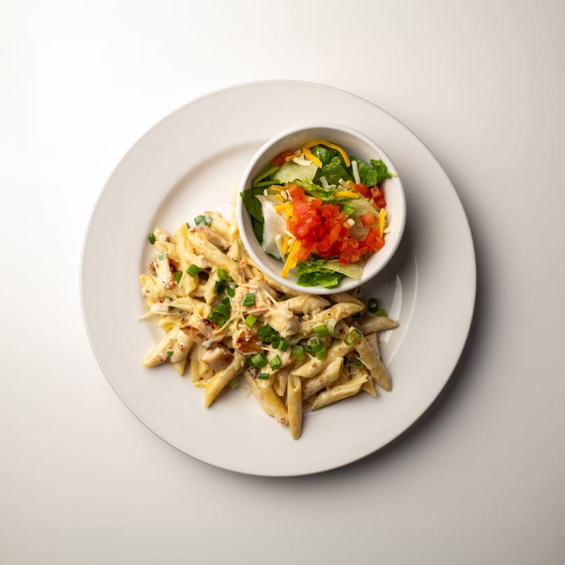 Creamy penne pasta with chicken and green onions, served with a side salad.