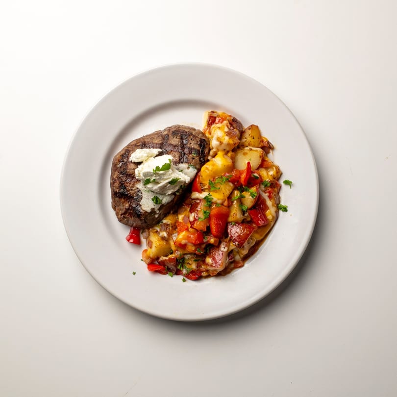 Grilled steak topped with white cheese and parsley, served with roasted potatoes and red peppers.