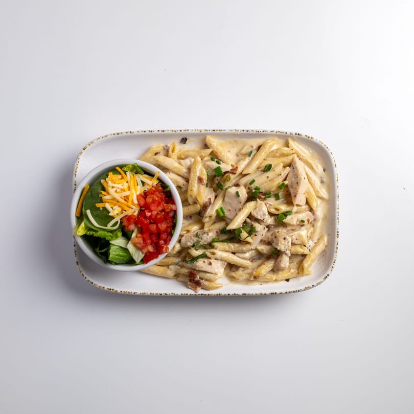 Creamy chicken penne pasta with a side salad topped with cheese and diced tomatoes.