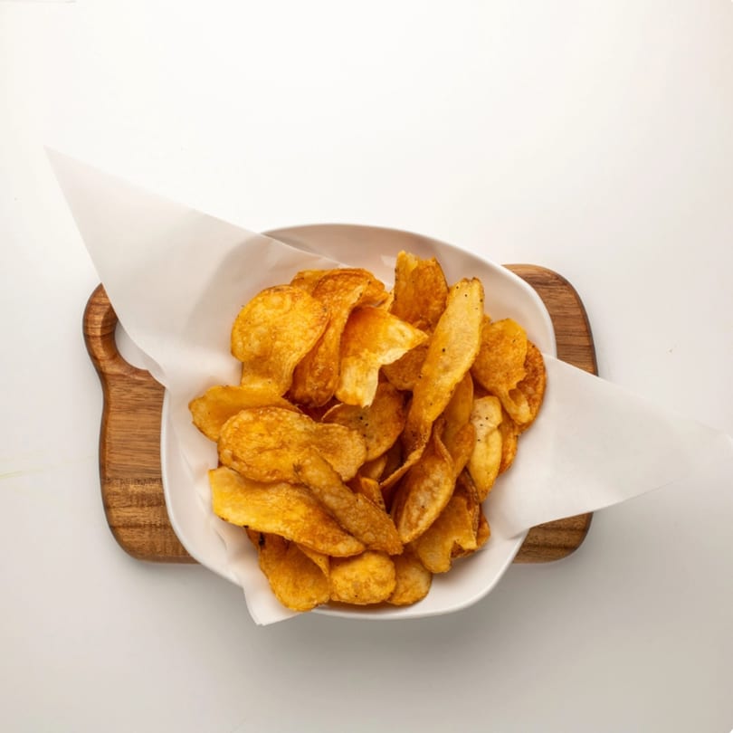 A white bowl filled with golden-brown, crispy Red Onion Cafe potato chips on a wooden board.